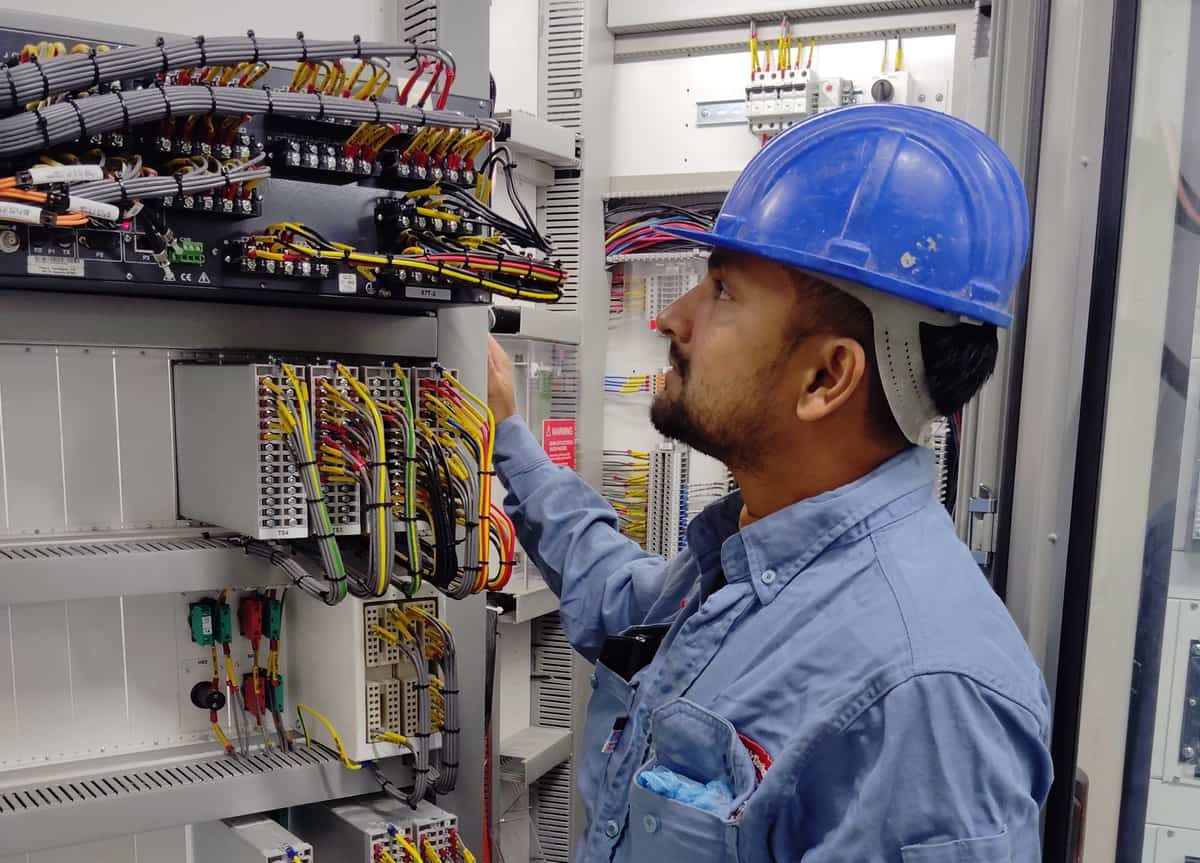 Technician inspecting labelled control-panel wires and terminal connections inside an electrical cabinet